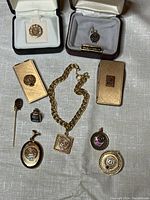 Display of all jewelry items with AT&T and SouthEastern Bell logos including money clips, pins, lockets, and a bracelet arranged on a cloth.