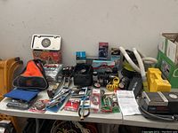 Full view of assorted car wash materials, jump starter cables, compressors, vacuums, and miscellaneous automotive accessories displayed on folding table.