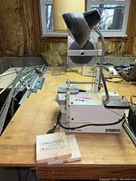 Front side view of the Diamond Tech International DL 1000 band saw with attached black adjustable lamp on wooden workbench in basement workshop.