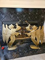Front view of both brass angels placed in front of a black marble fireplace, showing their full size and condition.