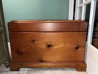 Front view of the wooden chest showing the wood grain and knots on the front panel, with base support visible at bottom.