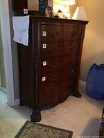 Front view of the Ashley Furniture 5 drawer chest showing dark wood, four visible metal drawer handles and carved rope detailing along vertical edge.