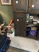 Wooden cabinet with doors partially open showing some storage bins and materials inside, and boxes on the floor beside it.