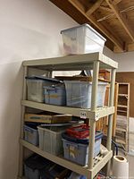 Four-tier plastic shelving unit holding multiple labeled and unlabeled bins of stained glass pieces