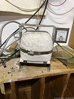 Front view of the Paragon tabletop kiln showing metal frame, white insulating body, wooden handles, and analog meter attached.