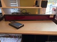 LED message board panel with red LED lights placed on a counter along with a handheld controller.