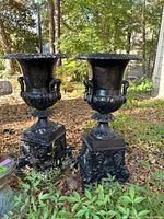 Two urns side by side outdoors on ground covered with leaves
