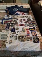 Overview of the laid out military patches, pins, medals and a folded blue cloth with emblem on bedspread