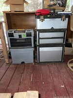 Two rolling toolboxes side by side on wooden floor, one Stanley metal with drawers, one MasterCraft plastic with compartments