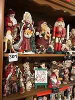 Full view of two shelves densely packed with various Santa Claus figurines, nutcracker, and holiday ornaments. Showcases a mix of traditional and Jim Shore styled figures.