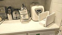 Countertop with Sunbeam Deluxe Mixmaster mixer, Sunbeam bread maker, Hardineeon toaster, and West Bend bread slicing guide