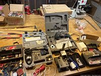 Wide view of workspace table showing multiple tool cases including rotary tool kits, chargers, and clamps arranged on table.
