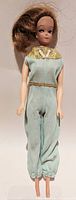 Front view of the 1960's brunette Barbie doll with pale blue-green jumpsuit and gold collar detail, showing dramatic eye makeup and brunette hairstyle.