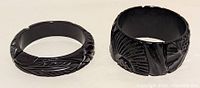 Two chunky black vintage Bakelite bracelets with carved floral and geometric details seen from the side and top angles.