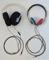 Photo showing two Koss KPH30i headphones side by side, black foam ear pads headphone has a straight black cord, the red and blue foam ear pads headphone has a braided silver-tone cord.