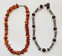 Two necklaces laid out on flat surface: one amber resin bead necklace and one glass and metal bead necklace.