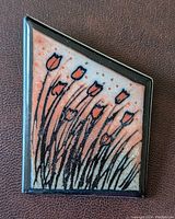 Front view of ceramic brooch showing hand-painted tulip design and black frame.