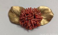 Close-up photo showing a coral and gold leaf brooch with vivid detailing on leaves and coral elements, clearly displaying its condition and design.