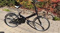 Side profile of black folding bicycle showing folding frame, saddle, pedals, and wheels.