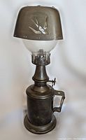 Full view of the vintage metal oil lamp with glass globe and engraved metal shade showing bird cutouts and overall structure.