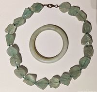 Full view of both chunky green glass bead necklace and jade bracelet bangle placed on white background.