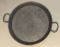 Top view of large round paella pan showing hammered textured surface and two side handles.