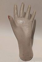 Front view of child-sized mannequin hand with visible crackled paint and vintage wear, thumb showing some red paint wear