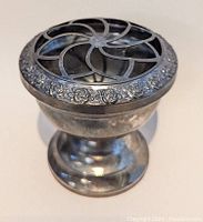 Angled side view of the pewter rose bowl flower frog showing pedestal base, rose pattern on the rim, and metal petal-shaped grid on top.
