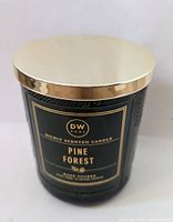 Front view of green textured glass jar with gold lid and black label showing DW Home Pine Forest scent.