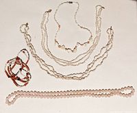 Multiple necklaces laid flat showing a variety of strings composed of seed pearls and pink coral beads. The pearls are small, round, and white, while the coral beads are pink and cylindrical. Clasp partially visible on some.