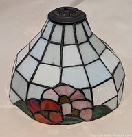Full view of the stained glass lampshade showing geometric white panels and floral design at the base in pink, red, and green glass.