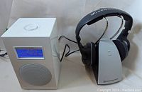 View of Tivoli speaker next to Sennheiser wireless headphones on charging base showing power on state with charging light illuminated.