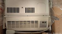 Front view of Haier window air conditioner showing vent grille, control panel with digital display and buttons, power cord with switch visible.