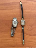 Two antique women's wristwatches placed side by side on wood surface, one with metal bracelet, one with cord strap.