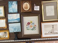 Overview photo showing multiple framed artworks including blue-toned wood pieces, embroidered flower picture, dried flower picture, pencil drawing, and watercolor landscapes.