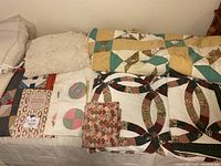 Seven quilts and a crocheted throw arranged on a bed, showing a variety of traditional pieced quilt patterns and colors.
