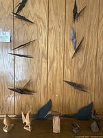 Wide view showing five carved natural wood bird figurines on surface below, with six dark painted carved wooden birds hanging against wood paneled background.