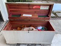 Open cedar chest showing white painted exterior, carved footed base, and interior cedar lining with assorted contents inside the chest.