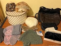 Multiple vintage hats, purses, and gloves displayed on a table including a round floral vintage hat box.