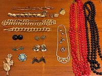 Photo showing overall lot contents including beaded necklaces, various bracelets, multiple pairs of earrings, and brooches arranged on wooden surface.