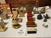 Top-down view of assorted miniature items including jewelry boxes, ships, carved figurines, and a red painted wooden box with Japanese designs.