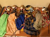 Front view of all six vintage Southeast Asian puppets showing different fabric costumes and detailed painted heads with sticks for arm movement.