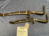 Both vintage ceremonial cutlasses laid side by side on dark fabric, showing full length with brass bands on dark wood sheaths.