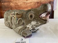 Front angle view of carved and painted wooden animal showing open mouth and facial details with visible cracks and wear.