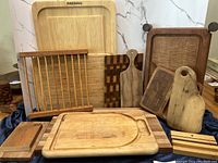 Photo showing 10 wood cutting boards and serving boards of various sizes and wood finishes arranged upright and overlapping.