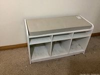 Front view of white laminate bench with seat pad and three open cubbies underneath. Shows minor dirt marks inside the cubbies.