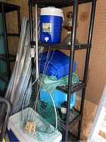 Shelf with Igloo cooler on top and various camping items below including fishing net and propane cylinder