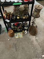 View of black tiered shelving unit holding multiple decorative items including the German wax candles, wood dolls, cloisonne vases and figurines.