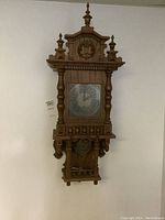 Full view of wall clock showing wood frame with finials and pendulum case