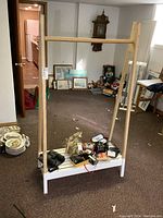 Full view of the wooden clothes rack in a room with various items on floor and background